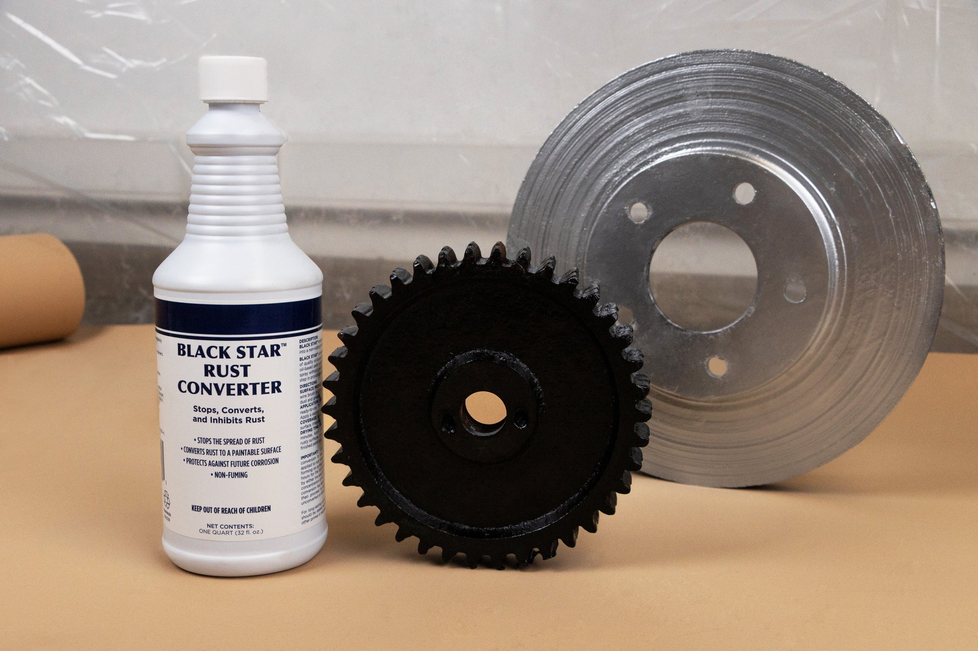 Bottle of Black Star Rust Converter displayed next to a restored black gear and a clean silver brake rotor