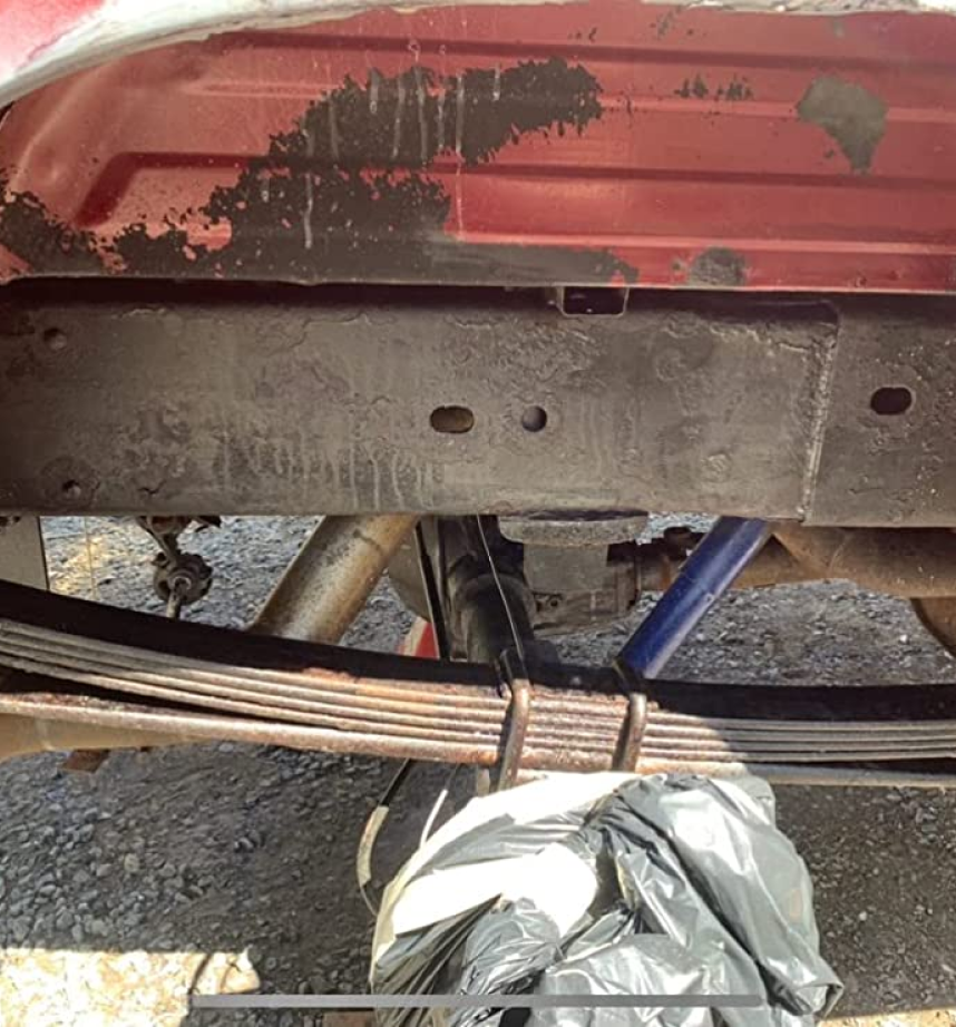 Undercarriage of a vehicle showing suspension components and frame, partially coated with black rust converter over previously rusted areas.