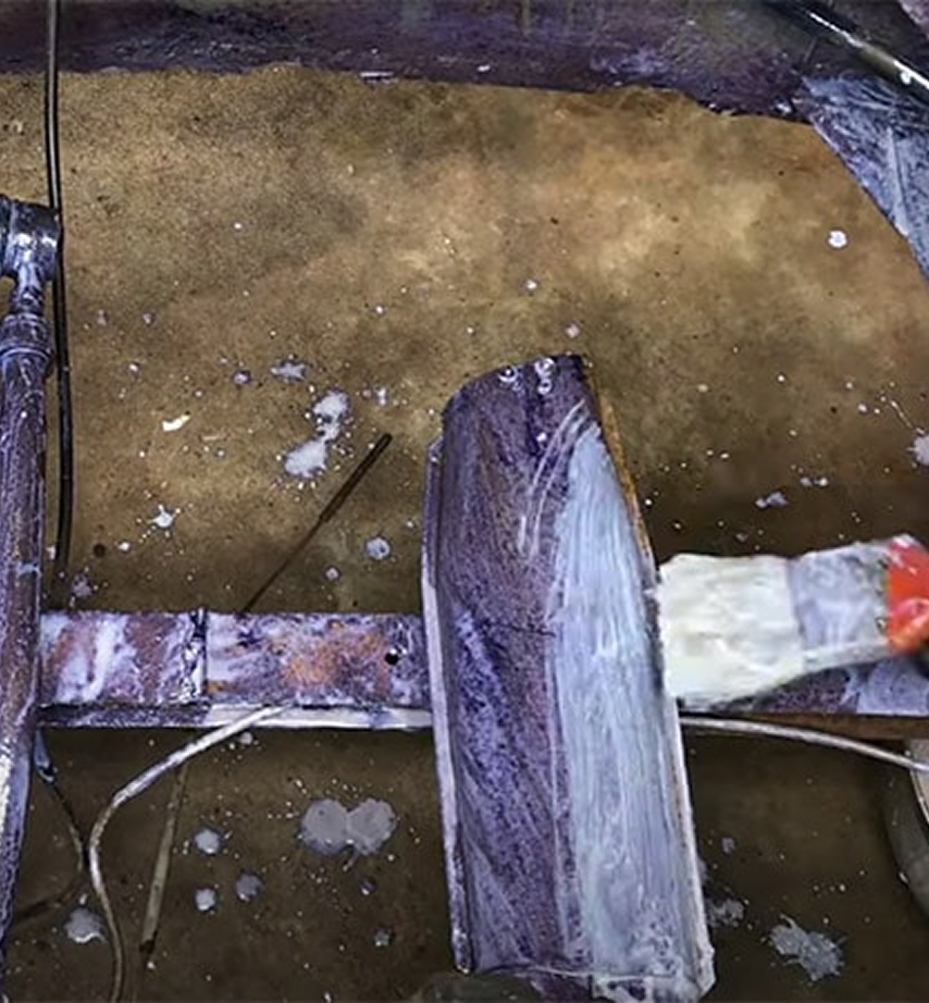 Close-up of a person applying a white coating, likely rust converter, with a brush onto a rusted metal surface.